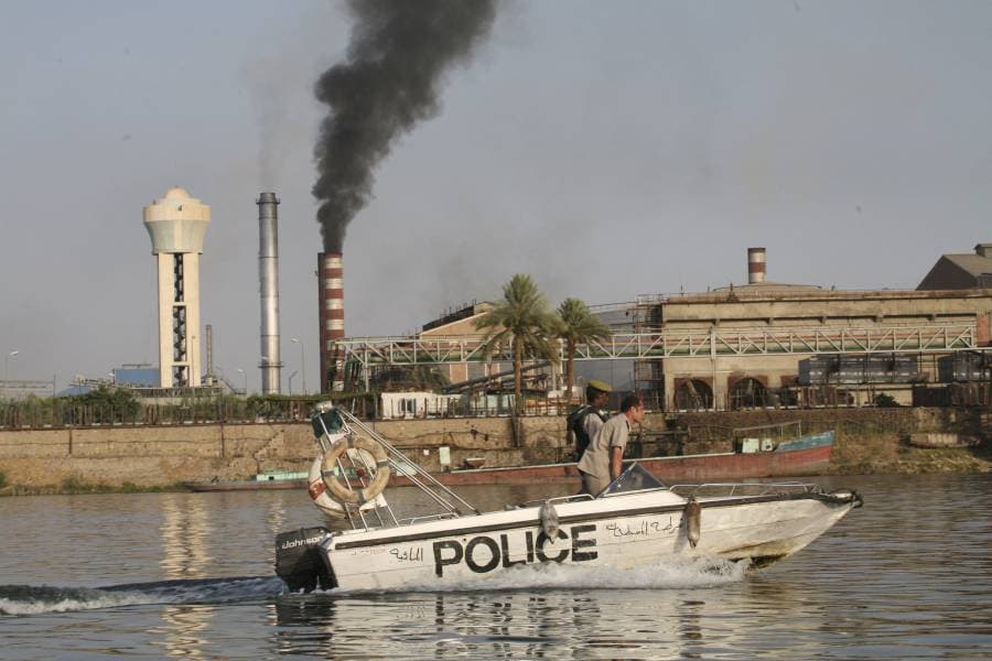 قارب يسير في مياه النيل وفي الخلفية فوهة مصنع يخرج منها عوادم