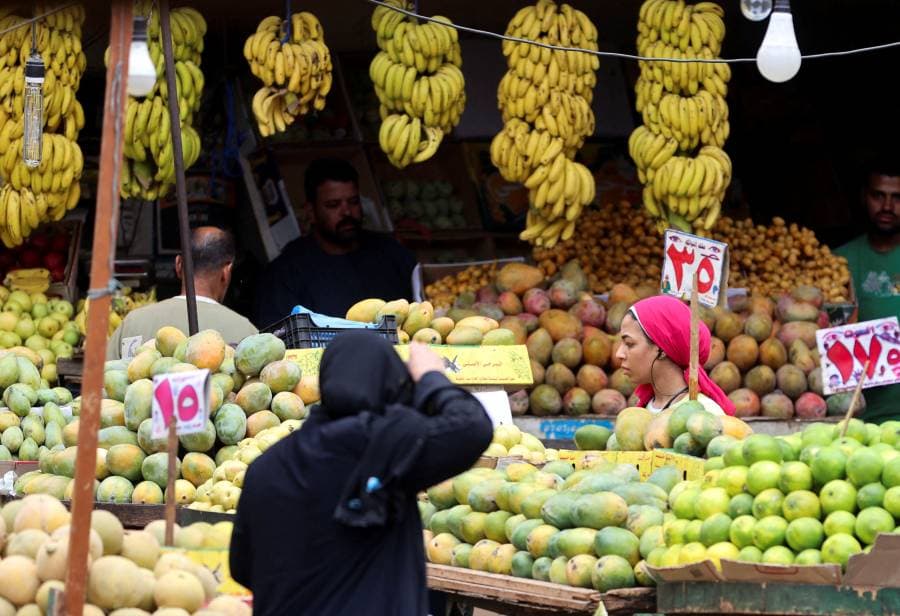 سيدة تقف أمام بائع للفاكهة في سوق شعبي بمصر