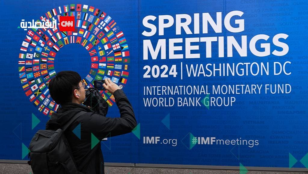 رجل يقف أمام مقر صندوق النقد ويصور لافتة الاجتماعات السنوية